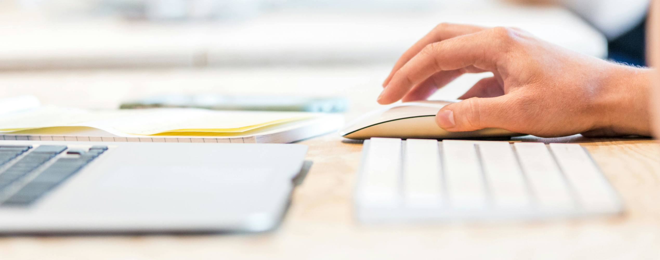 image of a desktop with a laptop, a keyboard and a hand holding a mouse.
